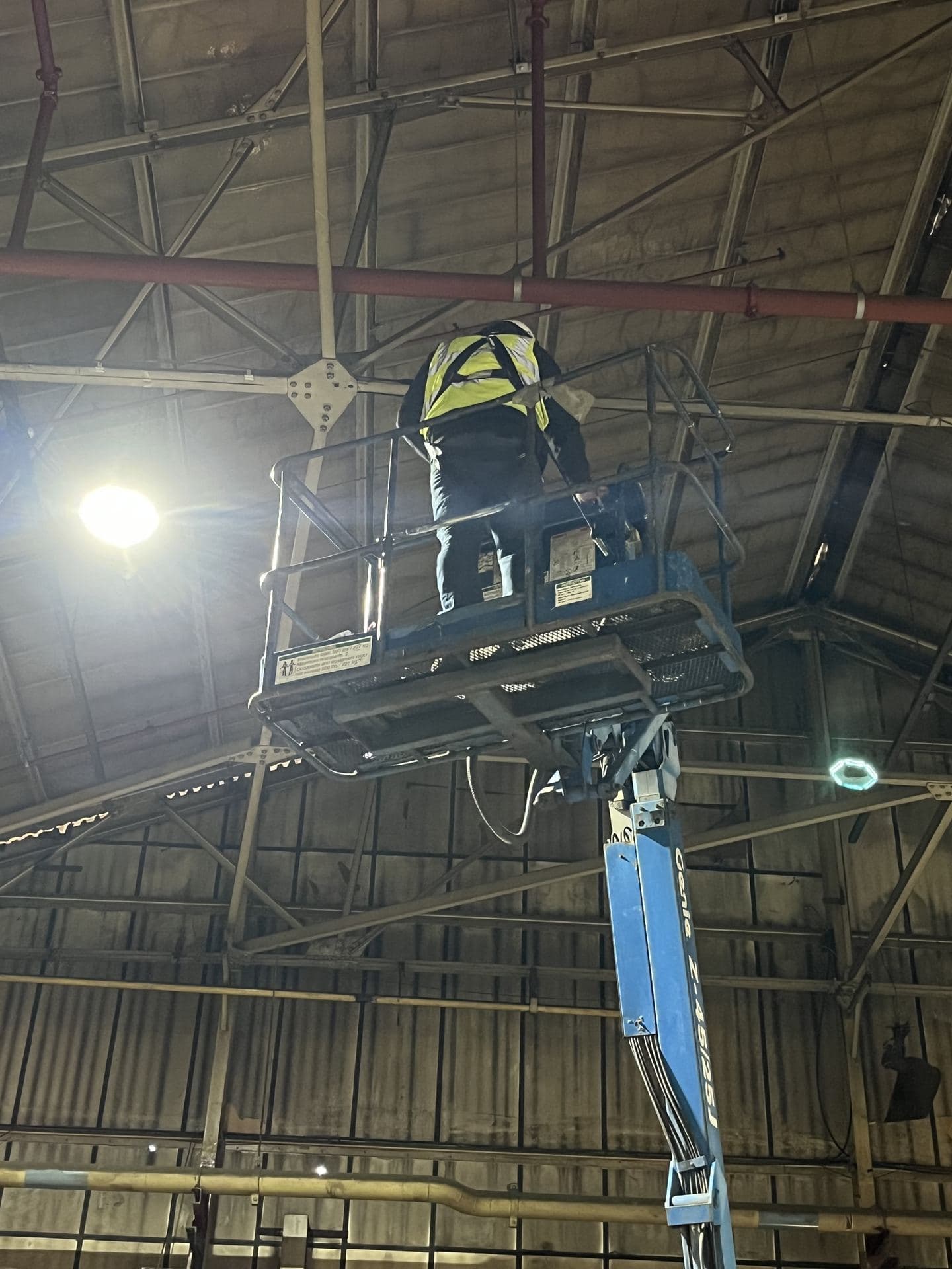 Engineer on a cherry picker running cable in a warehouse roof